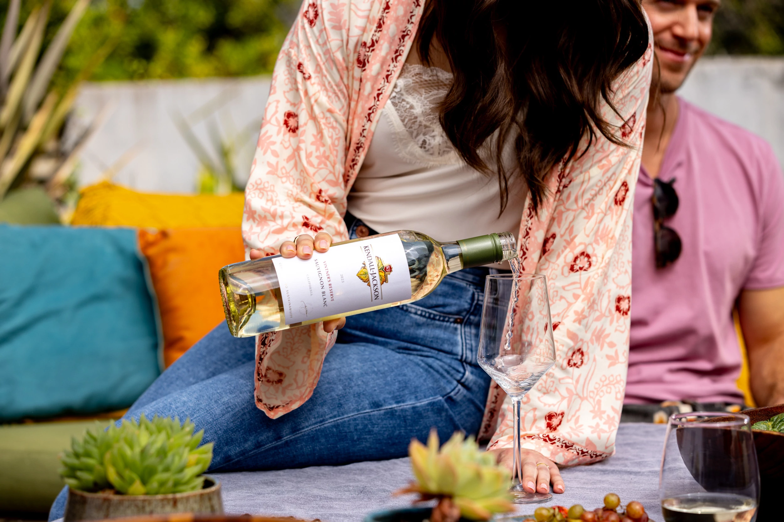 a woman sitting on a table pouring Kendall Jackson Sauvignon Blanc into a glass