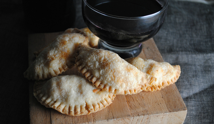 Empanadas on a cutting board with red wine