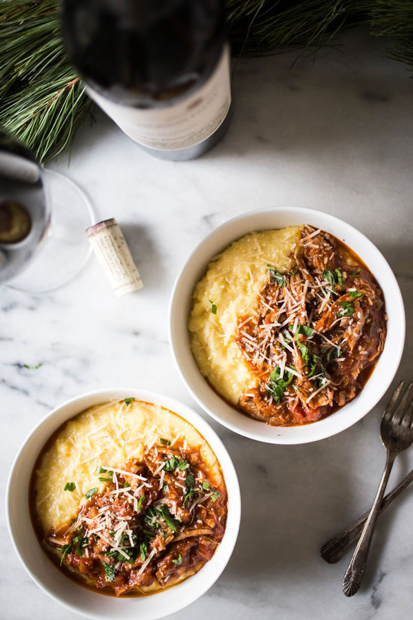 two bowls of pork ragu and polenta side by side with bottle of wine